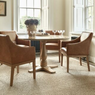 A dining table and dining chairs-dining room furniture-tan leather dining chair-round dining table-glassware-sisal rug-neutral walls-sideboard-dresser