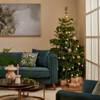 Living room featuring the Porter blue velvet sofa with a Christmas tree next to with elegant gold bauble, a set of nesting coffee table in a dark wood stain with gold legs.