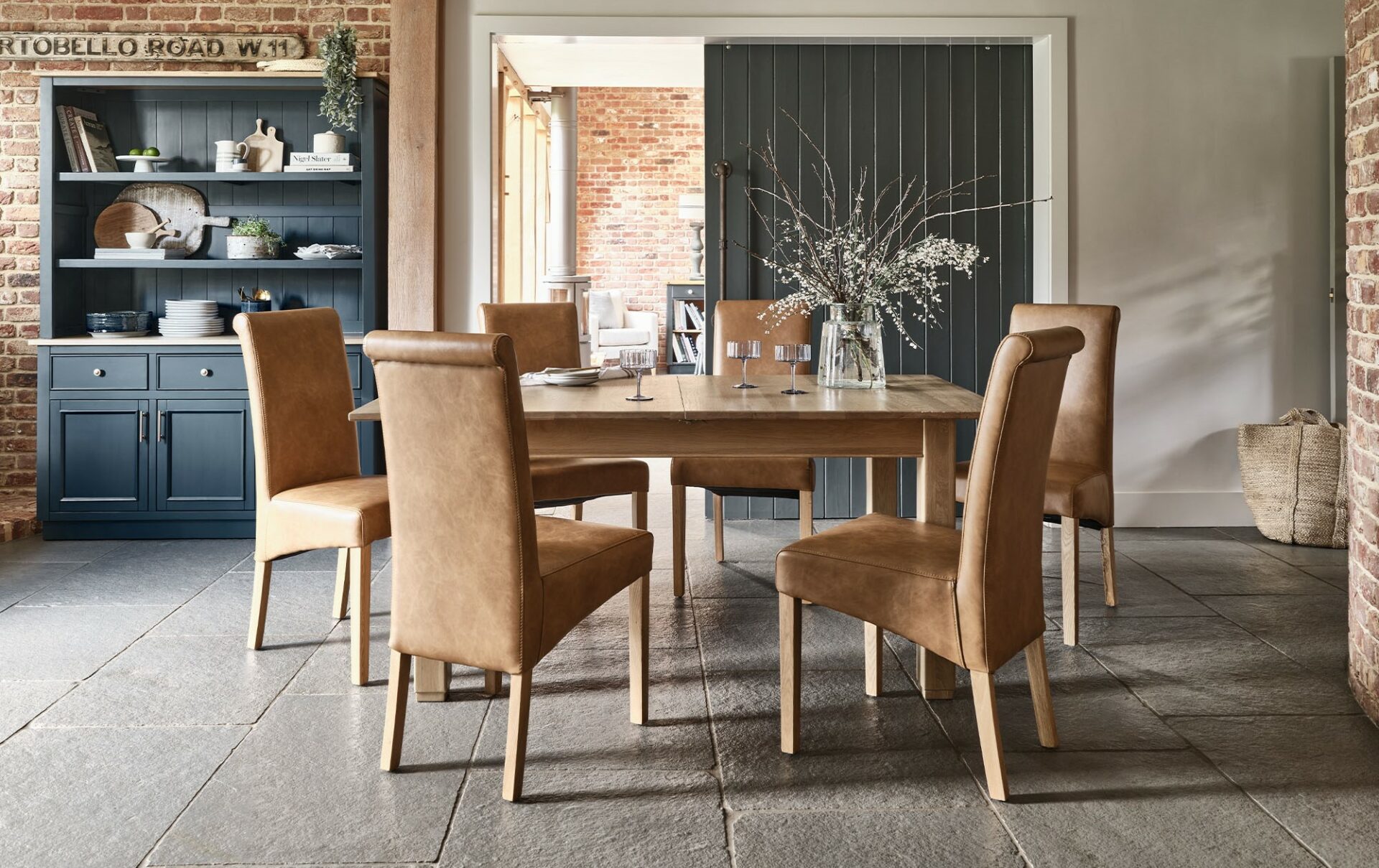 A kitchen table and chairs-kitchen dining furniture-extendable wooden table-tan leather effect seats-stone floor-dark blue dresser