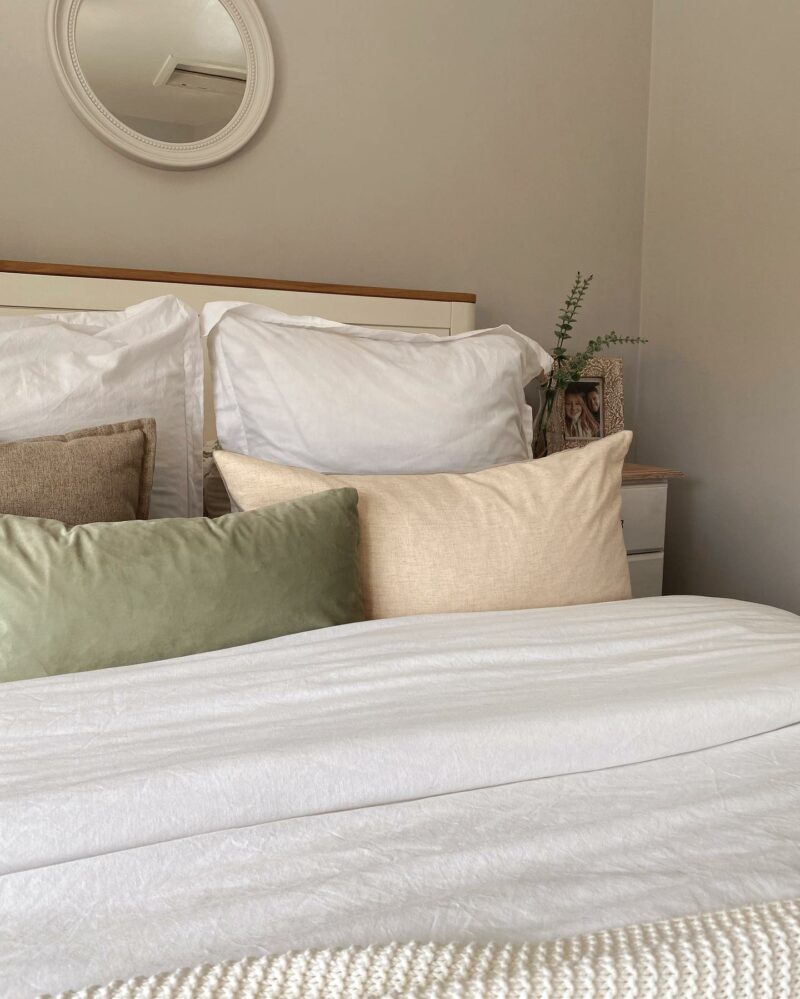 White bedding with pink and green cushions in a pale grey bedroom.