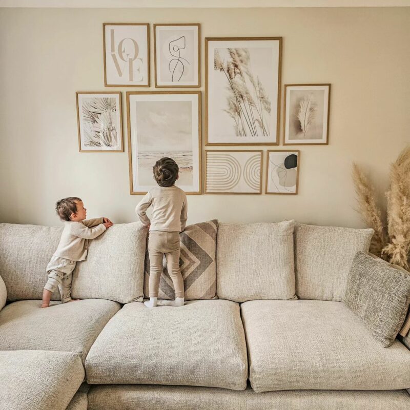 Cream corner cofa with muted gallery wall above and two young children looking up at the pictures.