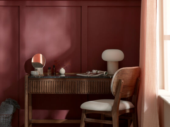 A dressing table and chair-bedroom furniture-burgundy walls-cream lamp-dark wooden dressing table-upholstered chair-wall panelling-pink curtain-jute rug