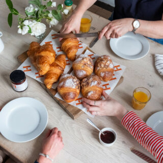 Pastries on a dining table-dining room-croissants-people sharing-orange juice-jam-chopping board-fresh flowers