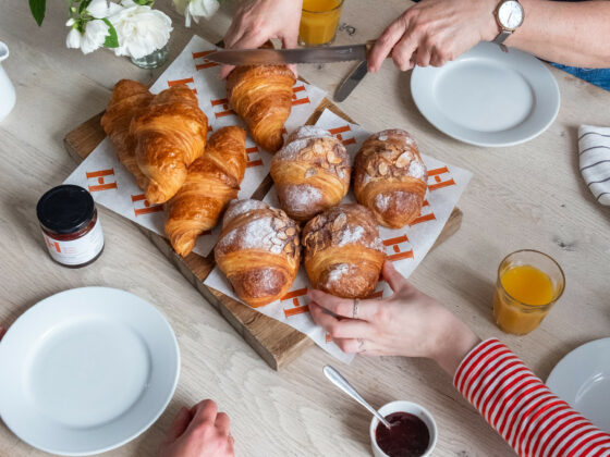 Pastries on a dining table-dining room-croissants-people sharing-orange juice-jam-chopping board-fresh flowers