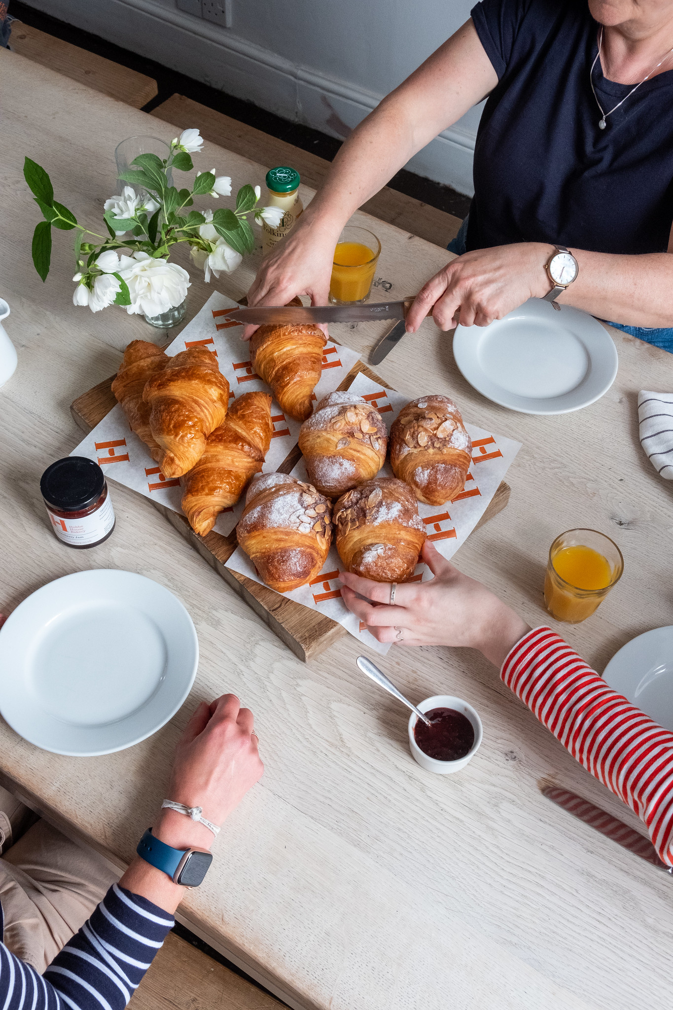 Pastries on a dining table-dining room-croissants-people sharing-orange juice-jam-chopping board-fresh flowers