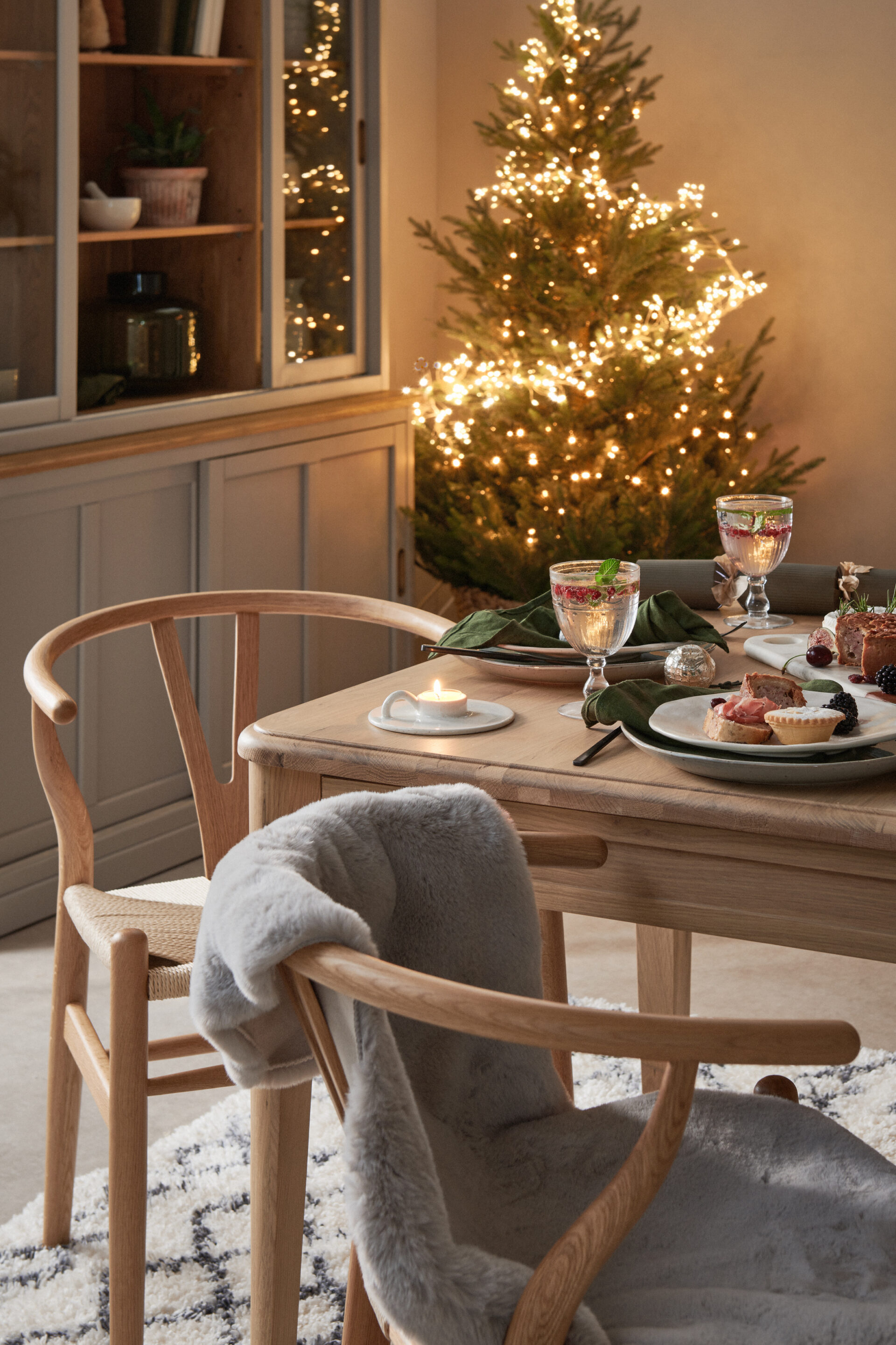 A dining table, dining chairs and dresser-dining room furniture-neutral walls-wooden dining table-wooden wishbone style dining chairs-textured rug-Christmas dining tablescape-scandinavian design-wooden grey mirror-Christmas fireplace-Christmas tree