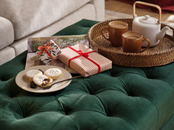 A sofa and footstool-living room furniture-yellow walls-velvet footstool-neutral cosy sofa-wicker tea tray-mince pies-wrapped presents