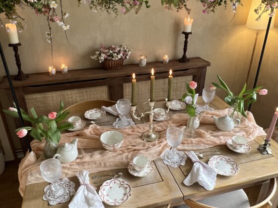 A dining table and chairs-dining room-vintage-style china-delicate glassware-white linen napkins-soft pink table runner-tulips in vases-lit candles-a floral arrangement with greenery and pastel flowers-wooden sideboard